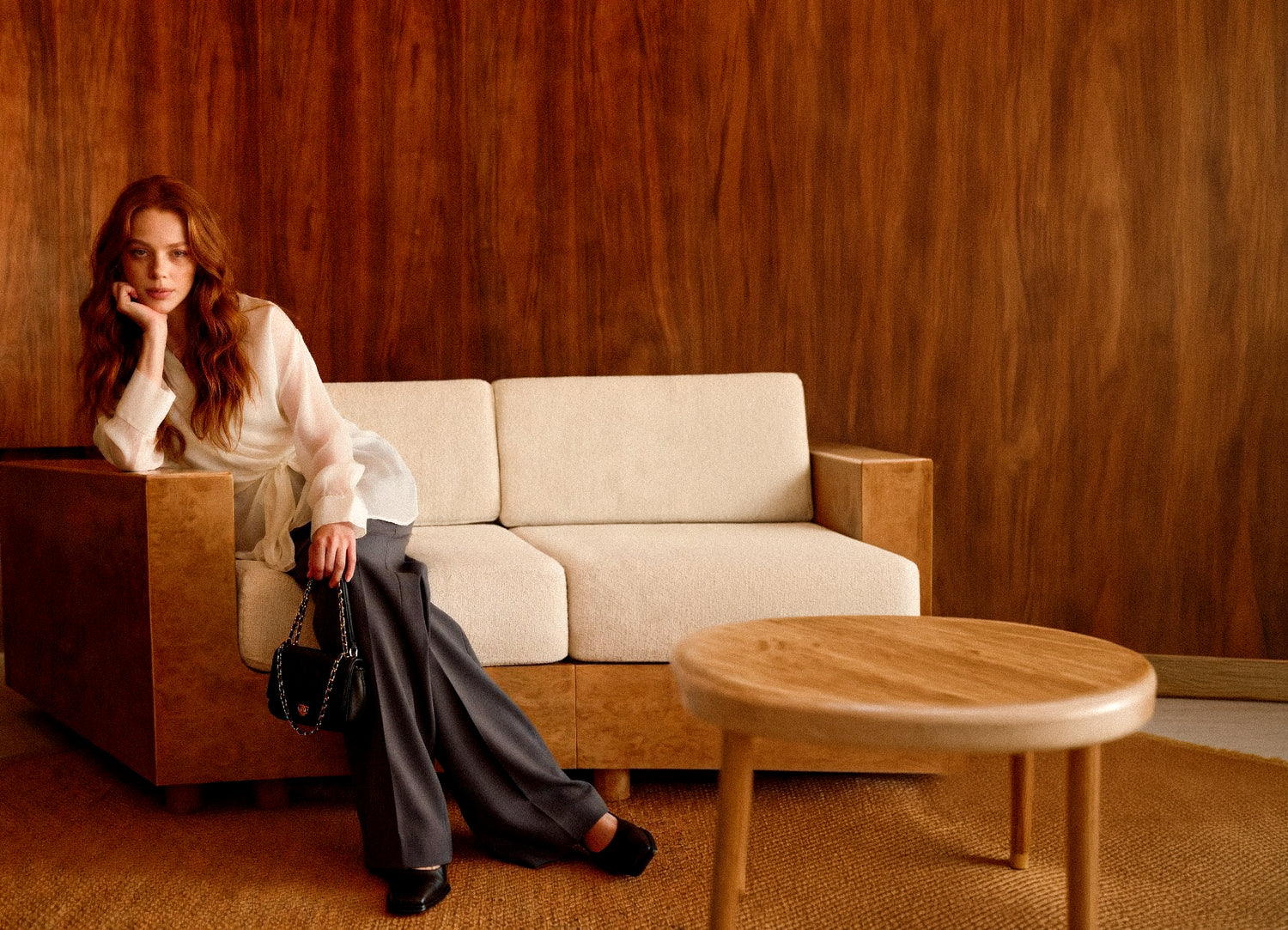 Woman sitting on a beige sofa in a room with wooden walls and a round wooden table wearing Adeptt Clothing.