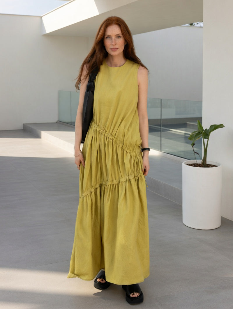 Woman in a yellow dress by Adeptt standing in a modern outdoor setting with a white wall and plant.