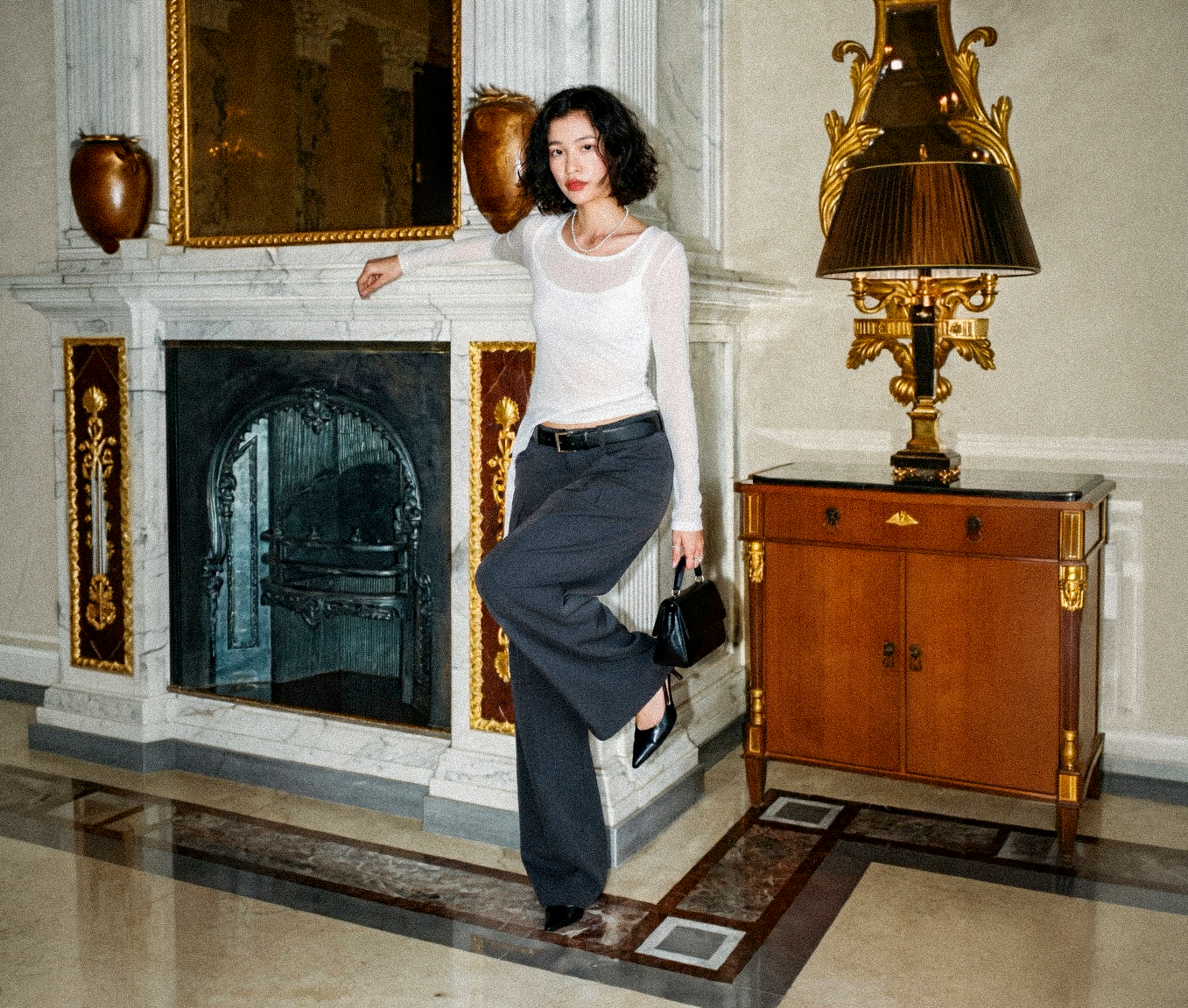 Woman posing in a grand room with decorative elements and a fireplace wearing Adeptt Clothing.